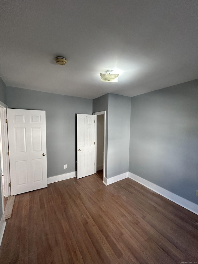 unfurnished bedroom with baseboards and dark wood-style flooring