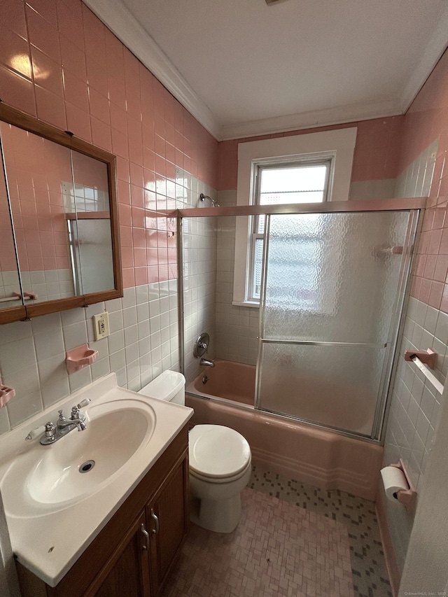 bathroom featuring toilet, ornamental molding, tile walls, bath / shower combo with glass door, and vanity