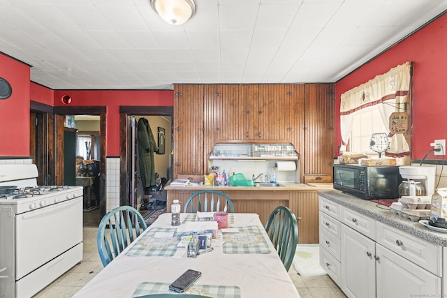 kitchen featuring gas range gas stove, light tile patterned flooring, light countertops, black microwave, and white cabinetry