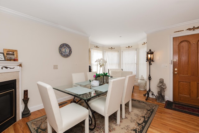 dining room with light wood-style floors, crown molding, a glass covered fireplace, and baseboards