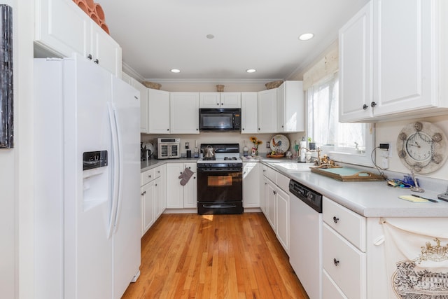 kitchen featuring light wood finished floors, light countertops, a sink, white appliances, and white cabinetry