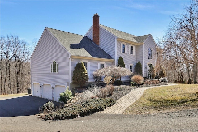 view of property exterior with roof with shingles, driveway, an attached garage, central AC, and a chimney