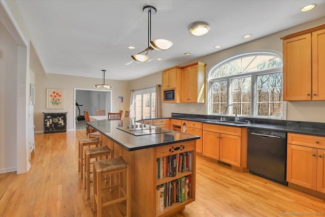 kitchen with a kitchen bar, black appliances, dark countertops, and light wood-type flooring