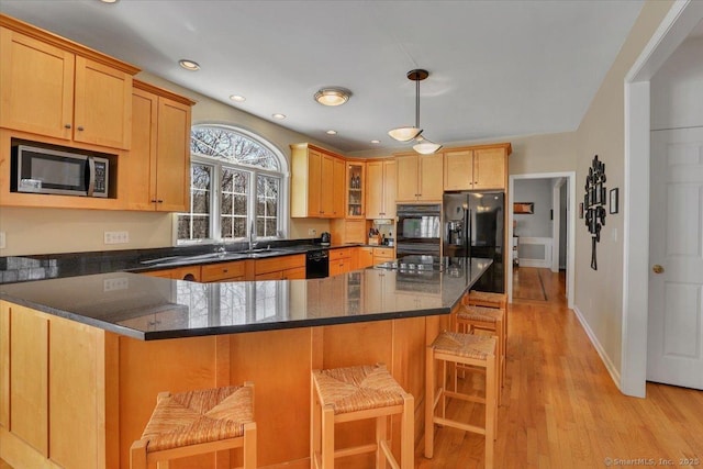 kitchen with a peninsula, dark stone counters, black appliances, a kitchen breakfast bar, and light wood-type flooring