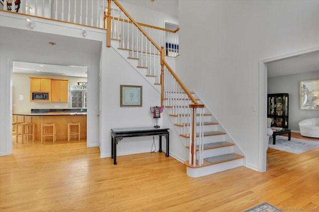 stairway featuring baseboards, wood finished floors, and a towering ceiling