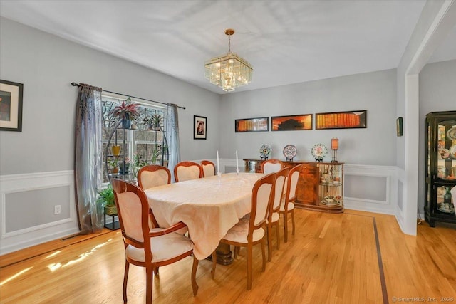 dining area featuring light wood-style flooring, a wainscoted wall, a chandelier, and a decorative wall