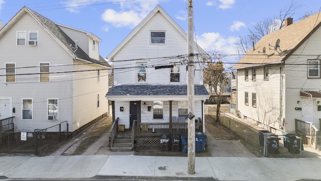 view of front facade with covered porch, a shingled roof, and fence