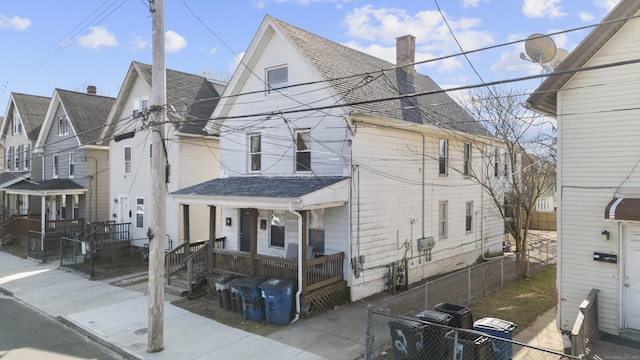 view of front facade featuring a chimney, a shingled roof, covered porch, and fence