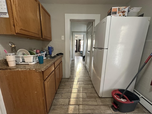 kitchen with backsplash, a sink, freestanding refrigerator, brown cabinets, and tile walls