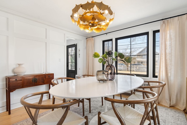 dining area with light wood finished floors, a decorative wall, crown molding, and a chandelier