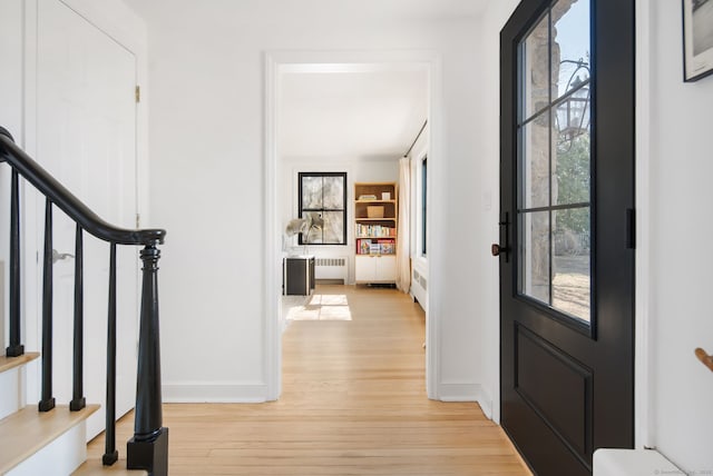 foyer entrance featuring stairs, radiator, baseboards, and light wood-type flooring