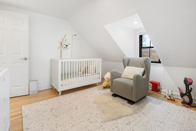 bedroom featuring baseboards, a nursery area, wood finished floors, and vaulted ceiling