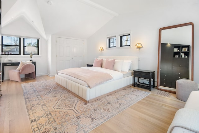 bedroom featuring lofted ceiling with beams, wood finished floors, a closet, and baseboards