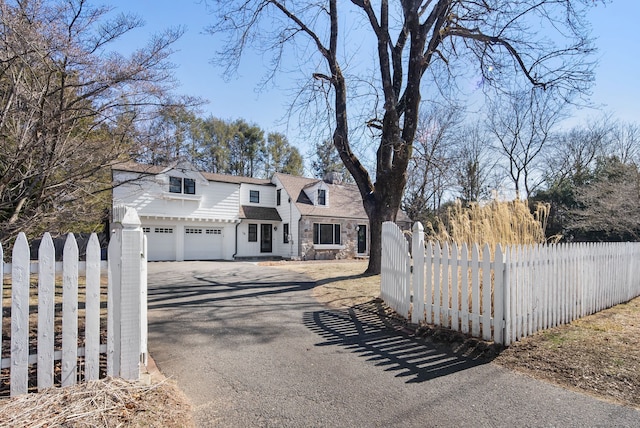 view of front facade featuring aphalt driveway, stone siding, and a fenced front yard