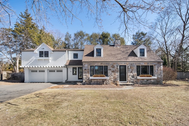 cape cod home featuring fence, driveway, roof with shingles, a front lawn, and stone siding