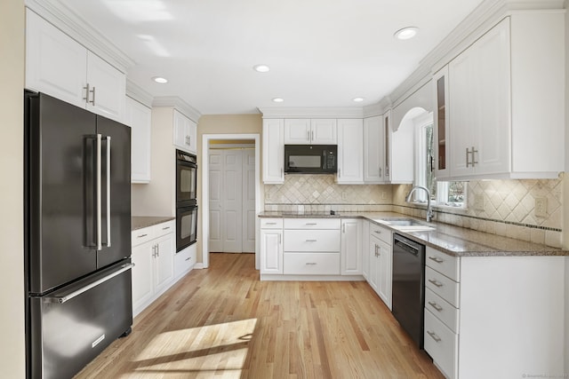 kitchen with light stone counters, a sink, black appliances, light wood-style floors, and white cabinetry