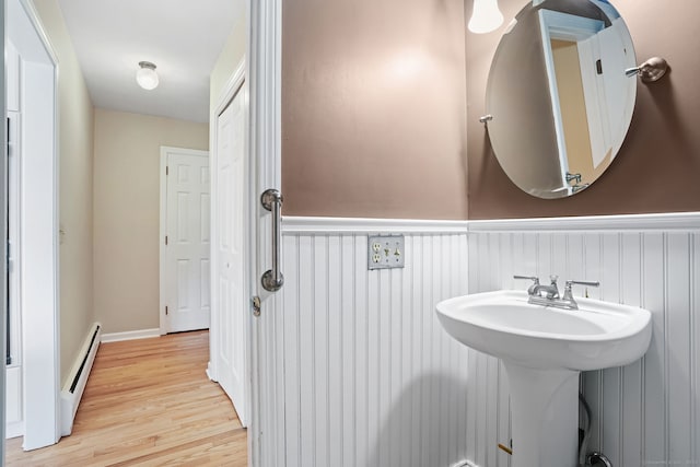 bathroom featuring a wainscoted wall, a baseboard radiator, a sink, and wood finished floors