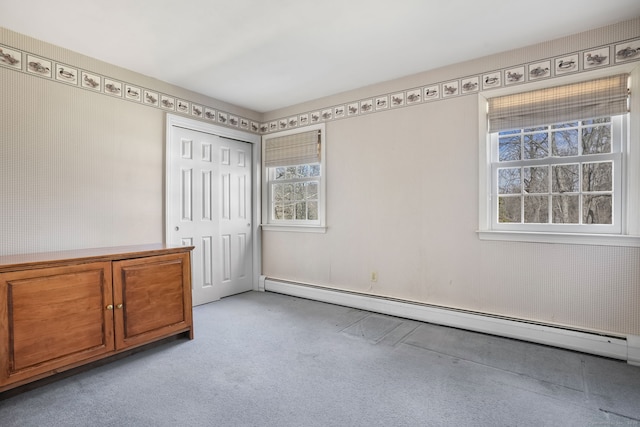 unfurnished bedroom with a baseboard heating unit, light colored carpet, and a closet