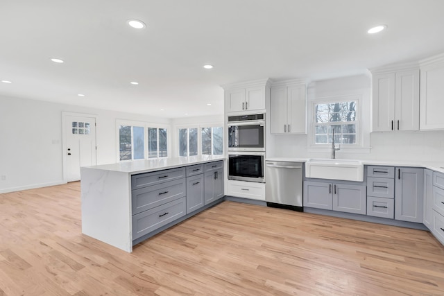 kitchen with light wood-style flooring, gray cabinets, a sink, stainless steel appliances, and a peninsula