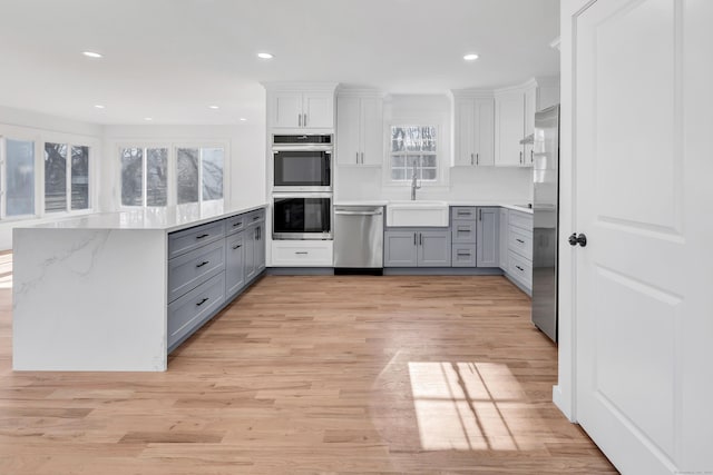 kitchen with a sink, appliances with stainless steel finishes, gray cabinetry, and light wood finished floors