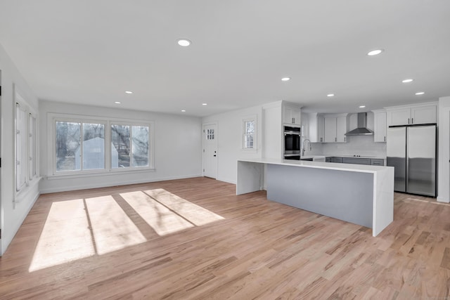 kitchen featuring wall chimney range hood, recessed lighting, appliances with stainless steel finishes, light wood finished floors, and light countertops