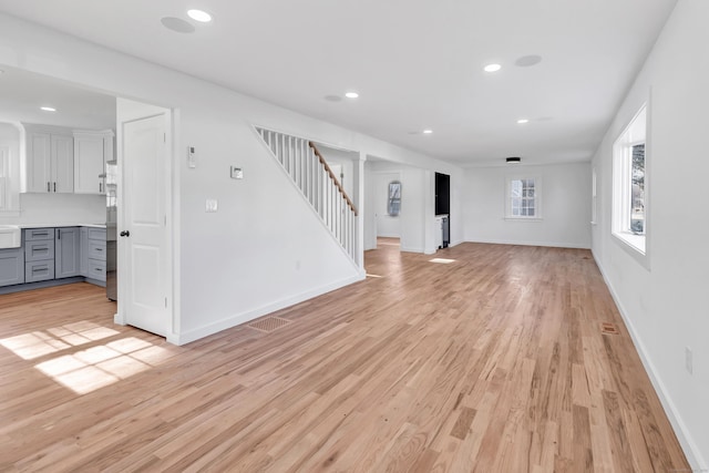 unfurnished living room with stairs, recessed lighting, light wood-type flooring, and baseboards