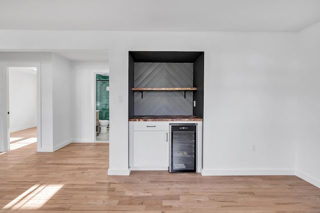 bar featuring baseboards, wine cooler, a dry bar, and light wood finished floors