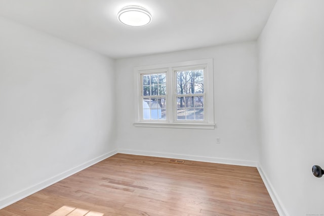 empty room with visible vents, light wood-type flooring, and baseboards