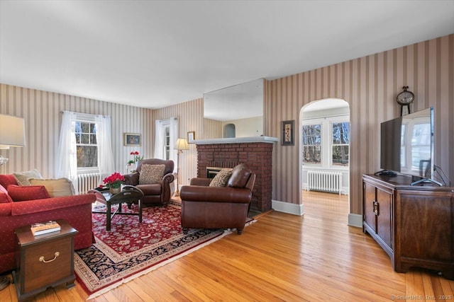 living area featuring light wood-style flooring, radiator heating unit, a fireplace, wallpapered walls, and baseboards