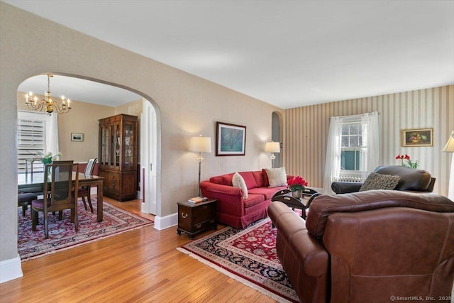 living room with light wood-style flooring, a notable chandelier, baseboards, and arched walkways