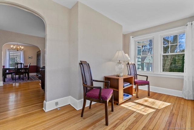 sitting room with light wood-type flooring, arched walkways, a notable chandelier, and baseboards