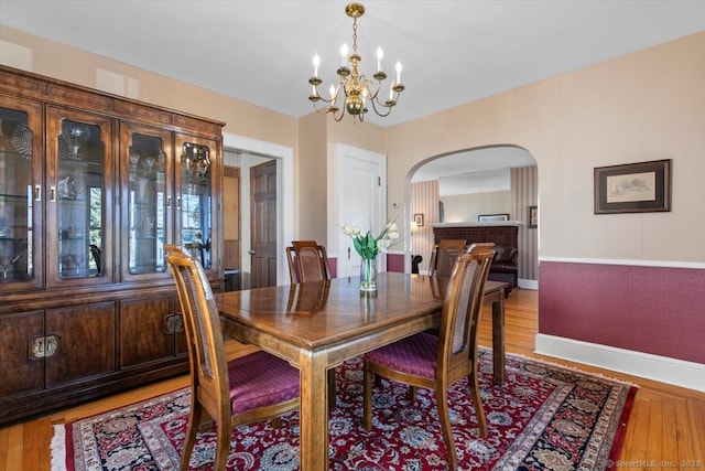 dining area with an inviting chandelier, wood finished floors, arched walkways, and baseboards