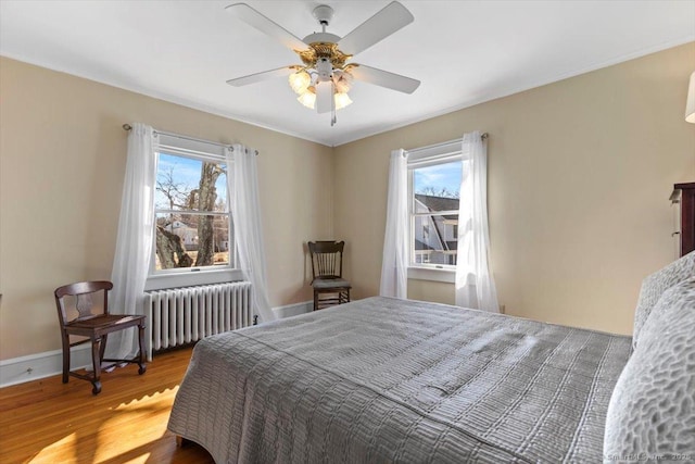 bedroom featuring radiator heating unit, wood finished floors, baseboards, and ceiling fan