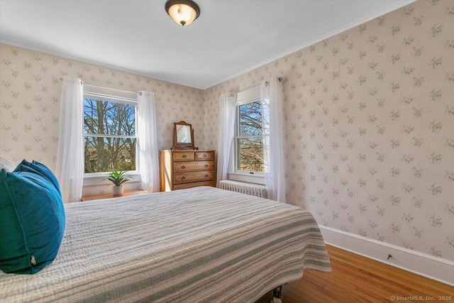 bedroom with wallpapered walls, radiator heating unit, wood finished floors, and baseboards