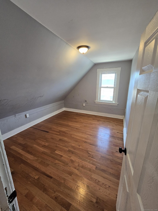 additional living space with dark wood-type flooring, baseboards, and vaulted ceiling