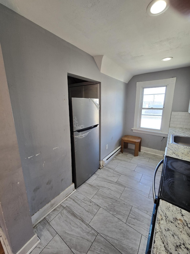 kitchen with baseboards, freestanding refrigerator, vaulted ceiling, black range with electric stovetop, and a baseboard heating unit