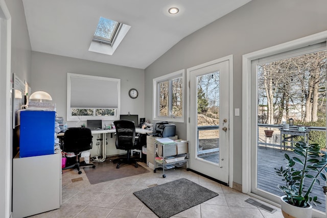 office space featuring vaulted ceiling with skylight, light tile patterned floors, a healthy amount of sunlight, and visible vents