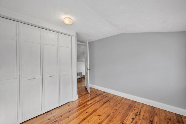 unfurnished bedroom featuring visible vents, baseboards, light wood-type flooring, lofted ceiling, and a closet