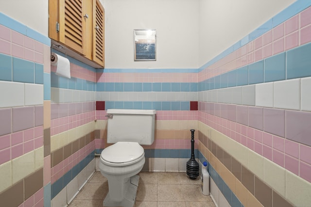 half bath with a wainscoted wall, toilet, tile walls, and tile patterned flooring