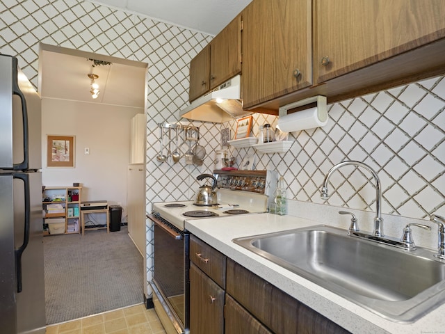 kitchen featuring electric stove, a sink, under cabinet range hood, freestanding refrigerator, and light countertops