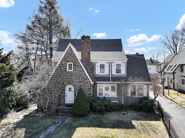 view of front facade with stone siding, a front yard, a chimney, and a shingled roof