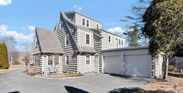 shingle-style home featuring an attached garage, a gambrel roof, driveway, and a shingled roof