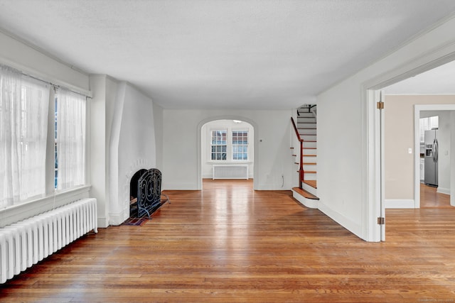 unfurnished living room with stairs, radiator heating unit, and wood finished floors