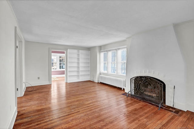 unfurnished living room with hardwood / wood-style floors, a wealth of natural light, a fireplace, and radiator heating unit