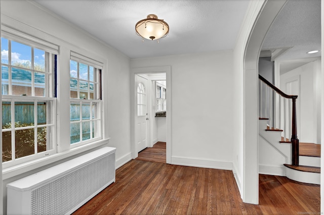 corridor with baseboards, wood-type flooring, radiator, and plenty of natural light