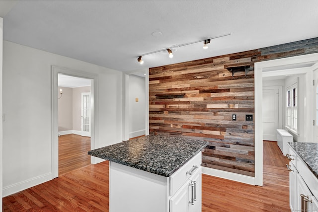 kitchen featuring wooden walls, baseboards, dark stone countertops, light wood-style floors, and white cabinets