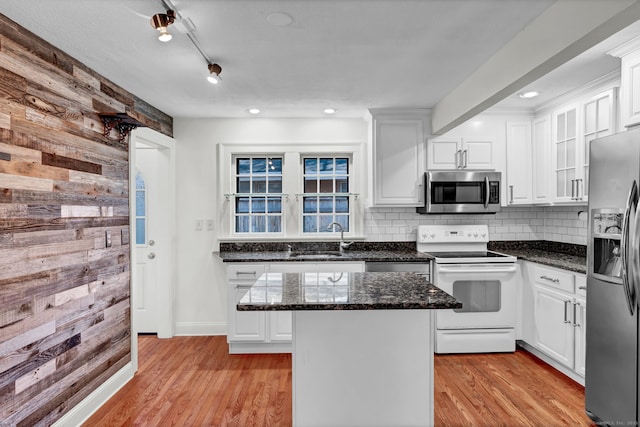 kitchen with light wood finished floors, wood walls, stainless steel appliances, and a sink