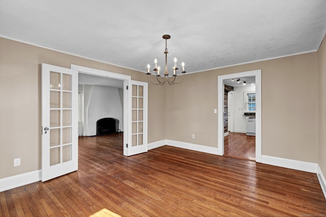 spare room featuring baseboards, ornamental molding, hardwood / wood-style floors, french doors, and an inviting chandelier