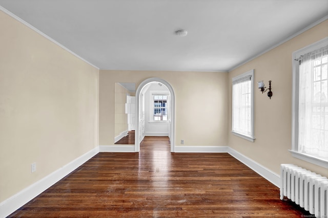 unfurnished room with baseboards, arched walkways, wood finished floors, and radiator heating unit