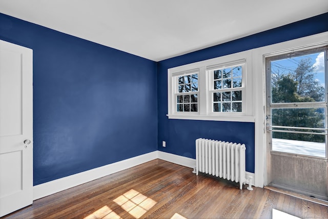 spare room featuring baseboards, radiator, and wood finished floors